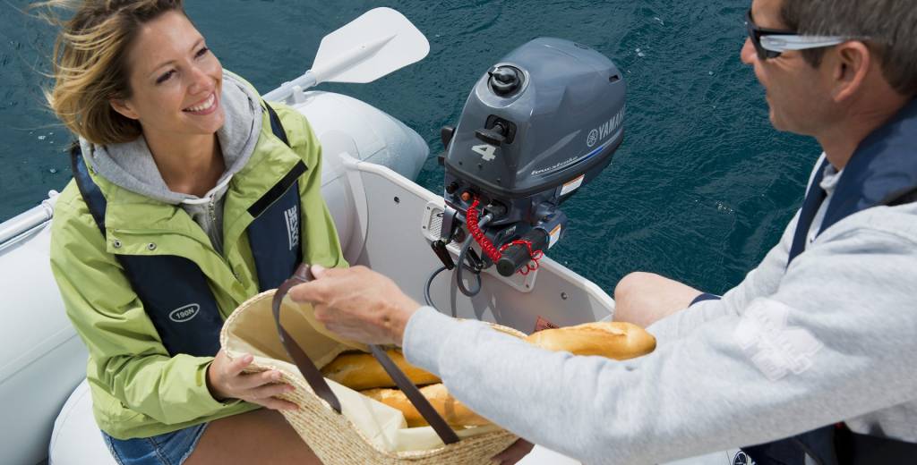 Yamaha 4 PK buitenboordmotor gemonteerd op een rubberboot, terwijl twee personen ontspannen varen en een mand met eten overhandigen op het water.
